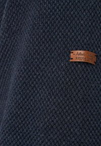 Marineblaues Strickgewebe mit einem strukturierten Muster, versehen mit einem braunen Lederetikett mit der Aufschrift "Authentic Clothing Redmond".
