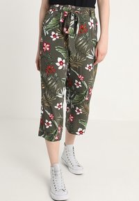 Cropped pants in olive green fabric featuring a floral pattern with red and white flowers, secured with a drawstring waistband.