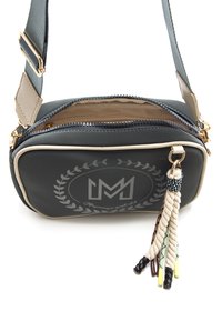 Schwarze und beige Umhängetasche mit Reißverschluss, verziert mit einer dekorativen Quaste und einem von einem Lorbeerkranz umgebenen Logo. Glatte Textur.