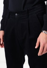 Dark navy corduroy trousers featuring a high-waisted design, pleats, and a button closure. The fabric has a ribbed texture.