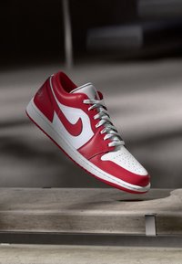 Sapatilha Nike vermelha e branca com atacadores suspensa acima de uma borda de betão em um ambiente pouco iluminado.