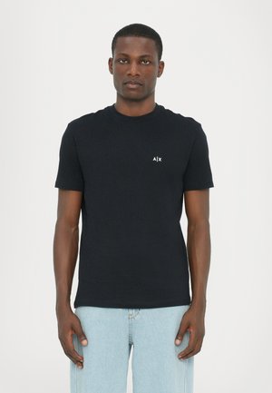 Black cotton t-shirt with a round neck and short sleeves. Features a small white logo on the left chest. Worn with light blue jeans.