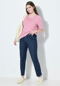 Růžové tričko s krátkým rukávem a výstřihem do V, tmavě modré džíny a světlé tenisky. Přes jedno rameno je přehozená vzorovaná taška.