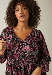 Robe à motifs floraux noirs avec décolleté en V, longues manches bouffantes et taille froncée, en tissu texturé dans des tons de rose.