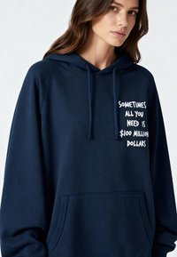 Sweat à capuche bleu marine en tissu doux avec une poche kangourou. Présente un texte imprimé en blanc : "Parfois, tout ce dont vous avez besoin, c'est de 100 millions de dollars."