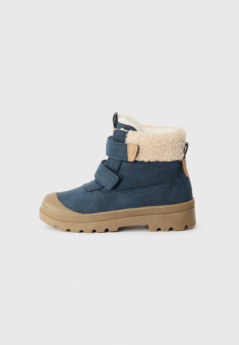 Boot in suede blu navy con due cinturini regolabili in velcro, suola beige e un morbido colletto in pelliccia sintetica beige per un maggiore calore.