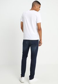 Hvit T-skjorte med korte ermer, bakfra, paret med mørkeblå jeans og hvite joggesko. Glatt stoff, tettsittende design, klassisk rund hals.