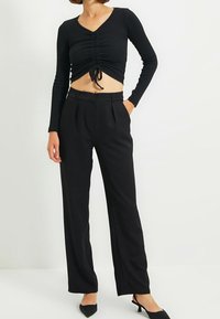 Czarny długi rękaw crop top z marszczeniami i sznurkiem, zestawiony z wysokim stanem, dopasowanymi czarnymi spodniami. Oba elementy mają gładką teksturę.
