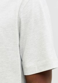 Heled hall lühikeste varrukate ja ümara kaelusega T-särk, mis on valmistatud pehmest puuvillasegust kangast, millel on sile tekstuur ja õmmeldud äär.