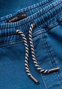 Pantaloni jogger in cotone blu con vita elastica, dotati di coulisse a righe nere e bianche con punte in metallo, etichetta visibile all'interno.