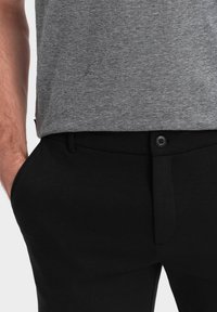 Grau strukturierter T-Shirt kombiniert mit schwarzen maßgeschneiderten Hosen, die über einen Knopfverschluss und einen ordentlichen Sitz verfügen. Nahaufnahme, die den Stoff und die Details betont.