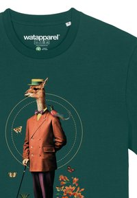 T-shirt vert foncé avec un design surréaliste : une girafe en costume marron, nœud papillon et chapeau, entourée de papillons et de fleurs.