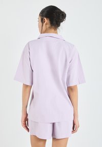 Lavender short-sleeve shirt with a collar, made of lightweight fabric. Features a relaxed fit and subtle sheen. Paired with matching shorts.