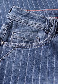 Jeans de mezclilla azul con rayas blancas verticales, que presentan una cinturilla acolchada, costuras en contraste y un pequeño detalle en el bolsillo trasero.