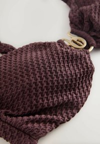 Brązowa tkanina o fakturowanym wzorze z złotą okrągłą klamrą. Miękki, układający się materiał o luźnym, marszczonym kroju i połysku.