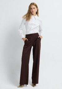 Witte button-up shirt met een gestructureerde kraag, gecombineerd met bruine broek met pinstripes en wijde benen. Schoenen zijn metallic goud met een spitse neus.