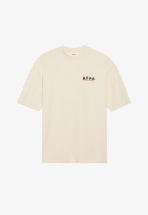 T-shirt en coton couleur crème, à manches courtes, avec un col rond et un motif imprimé en noir et rouge sur le côté gauche de la poitrine.