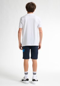 Bílá košile s krátkým rukávem, námořnické šortky s modrou náprsní kapsou, bílo-černé tenisky a černo-bílé pruhované ponožky.