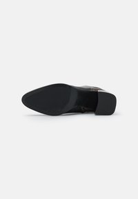 Czarna podeszwa buta z ostrym noskiem na obcasie blokowym, widziana od spodu na jednolitym białym tle.