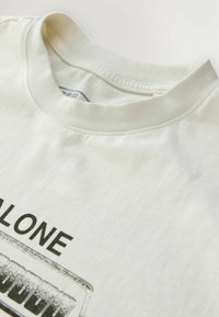 Off-white crewneck t-shirt med sort tekst "ALONE" og et gråtonet grafik af et kassettebånd på forsiden.