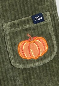 Grüner Cord-Stoff mit einer Vordertasche, die eine orangefarbene Kürbis-Stickerei und ein blaues Etikett mit der Aufschrift "Jojo" zeigt. Strukturierte Oberfläche und geripptes Muster.