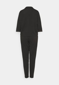 Tylny widok czarnego zestawu składającego się z dwóch części: żakietu z rękawami 3/4 oraz spodni zwężanych, na białym tle.