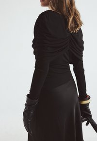 Musthave musta pika varrukasüdamik tagaküljel klappide detailidega, kombineeritud mustade nahkkindade ja sujuva musta seelikuga.