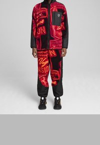 Red and black fleece zip-up jacket with neon pattern; matching pants featuring graphics. Black accents and logo on chest pocket.