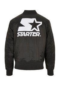 Veste bomber noire en tissu lisse, avec un grand logo "S" blanc et un motif d'étoile au dos. Manches texturées et poignets côtelés.