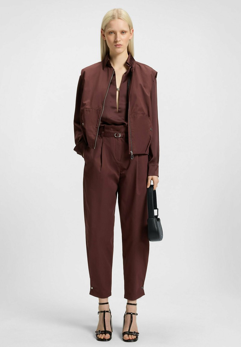 Tenue bordeaux avec un gilet zippé et un pantalon assorti. Comprend une taille ceinturée, une coupe élégante et un petit sac à main noir. Sandales à talons hauts avec lanières.