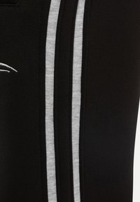 Czarne spodenki sportowe z szarymi paskami po bokach, wykonane z miękkiego, rozciągliwego materiału. Posiadają subtelne logo w pobliżu pasa.