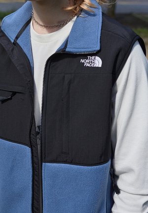 Schwarze und blaue Fleeceweste mit Reißverschluss, Stofftaschen und Steppnähten. Verfügt über ein Logo auf der Brust und ein hochstehendes Kragendesign.