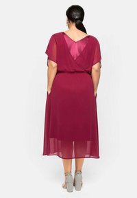 Robe en chiffon bordeaux avec un dos en V, des manches courtes évasées, et des poches latérales, présentant une silhouette fluide et une longueur jusqu'au genou.