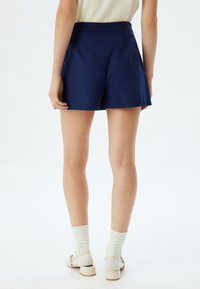 Marineblauwe shorts met een op maat gemaakte uitstraling, voorzien van een platte voorkant, zakken en een licht uitlopende zoom. Glad materiaal met een gestructureerde pasvorm.