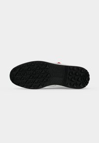 Semelle de chaussure en caoutchouc noir avec motifs triangulaires de la bande de roulement, conçue pour l'adhérence et la traction, présentée sur un fond blanc uni.