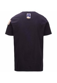 Maglietta nera con maniche corte, caratterizzata da un logo bianco e blu sul retro e da una toppa della bandiera americana con dettagli arancioni sulla manica sinistra.