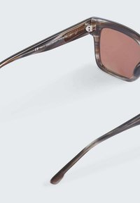 Lunettes de soleil avec des verres teintés marron, monture en écaille de tortue claire, forme élégante et détail métallique sur les charnières. Comprend le numéro de modèle sur le côté.