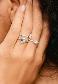 Sterling silver -renka: yksi esittää simpukka-kuvioita, toinen sydäntä ja kolmas kalaa, kaikilla on sileä ja kiillotettu pinta.