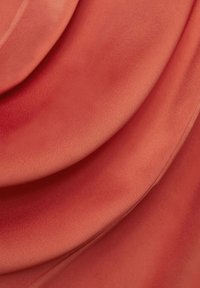 Tissu doux et froissé dans une teinte corail chaude, présentant une texture lisse et de douces plis drapés, mettant en valeur ses qualités légères et fluides.