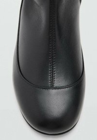 Zapato de cuero negro con un acabado suave, punta redondeada y un sutil detalle de costura a lo largo de la parte superior. Diseño minimalista sin hardware visible.