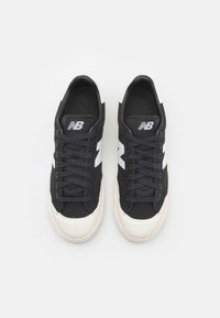 Pari mustia ja valkoisia New Balance -lenkkareita nauhoilla, näkymä päältä vaaleanharmaalla taustalla.