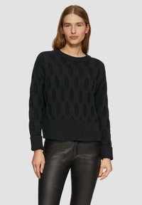 Maglione nero a maglia con un motivo testurizzato e ritagli ovali, scollo tondo e polsini a coste. Abbinato a pantaloni in pelle neri.