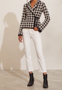 Neuleperhonen takki musta ja kerma houndstooth-kuviossa, jossa on ylellinen kaulus ja musta reunus, yhdistetty valkoisiin lyhyisiin farkkuihin ja mustiin nilkkabootseihin.