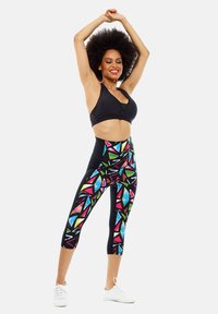 Sujetador deportivo negro con cuello redondo, combinado con leggings de talle alto de estampado geométrico multicolor, que exhiben patrones y texturas vibrantes.