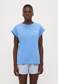 Blauwe katoenen t-shirt met omgeslagen korte mouwen, met voorop de tekst "Daydreamer." Gepaard met witte shorts met blauwe strepen.