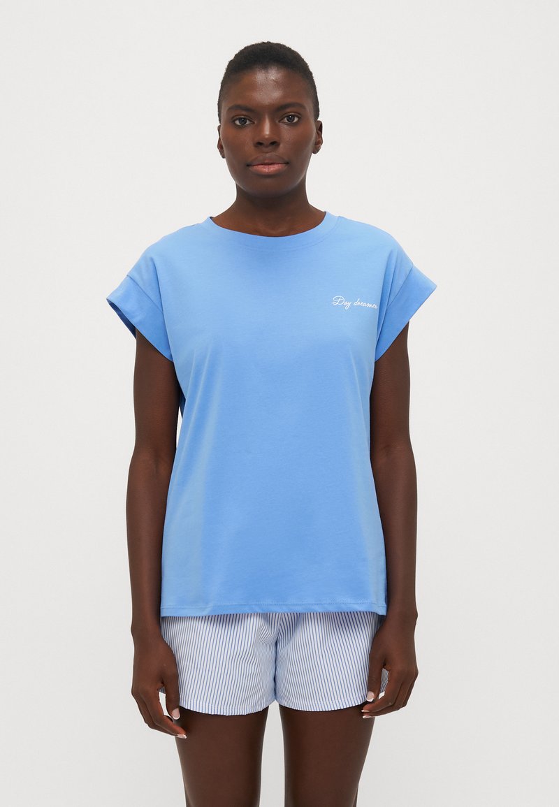 Blauwe katoenen t-shirt met omgeslagen korte mouwen, met voorop de tekst "Daydreamer." Gepaard met witte shorts met blauwe strepen.