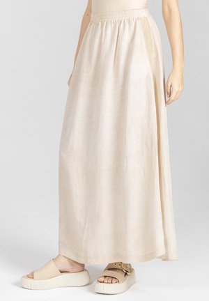 Beżowa spódnica do kostek z elastycznym pasem noszona z beżowymi sandałami na platformie na szarym tle.