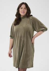Olijfgroene, ribbelige corduroy jurk met een hoge hals, ellebooglange pofmouwen en zijzakken. Zachte textuur en een ontspannen pasvorm.