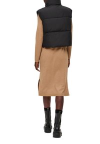Zwarte gewatteerde mouwloze vest over een beige jurk tot op de knie met zijsplitten, gecombineerd met zwarte enkellaarsjes met dikke zolen.