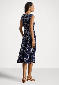 Marineblå blomsterkjole med tettsittende overdel og utsvingt skjørt. Laget av lett stoff, med hvite blomsterutskrifter og ermelaust design.